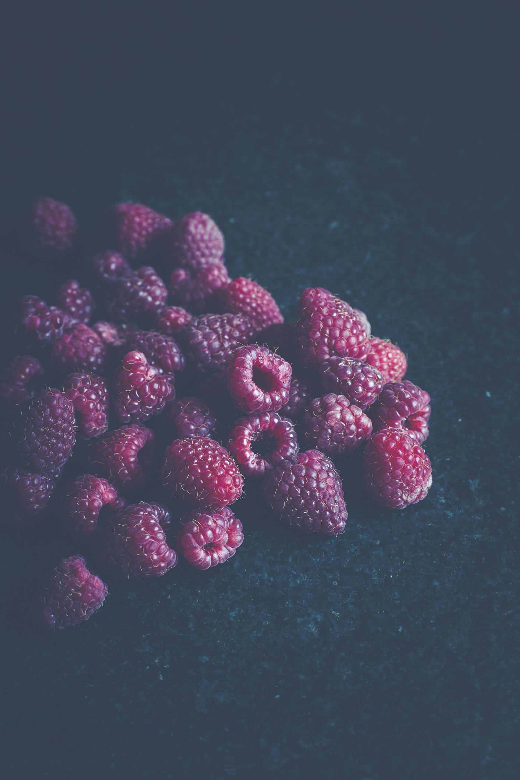 Close-up of fresh ripe raspberries on a dark textured surface, showcasing vibrant colors and natural textures.