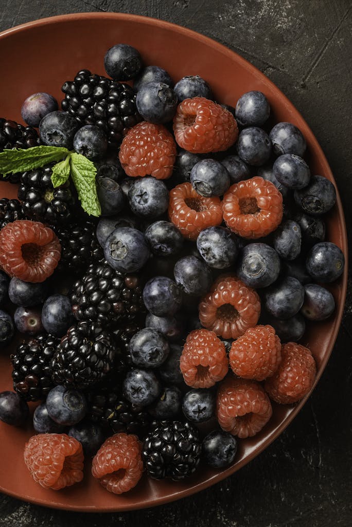 Fresh blackberries, blueberries, and raspberries on a red plate from above.